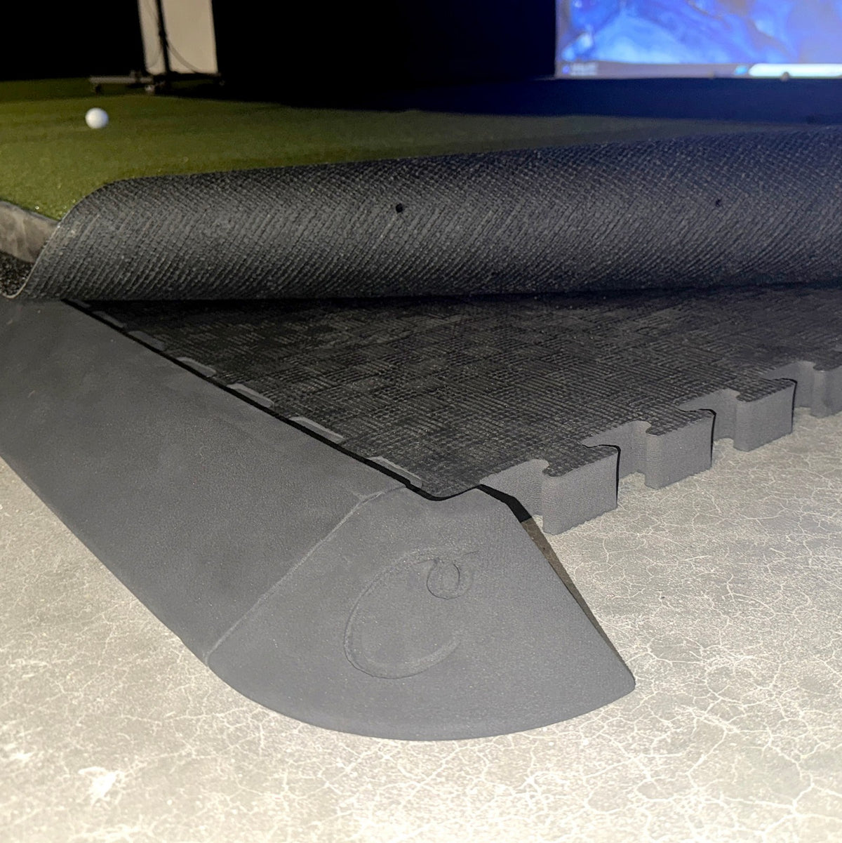Tapered edge piece holding turf flush against a golf room floor tile subfloor